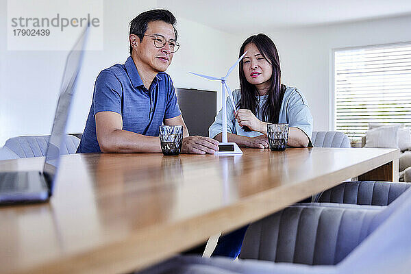 Smiling freelancers with wind turbine model sitting at table in living room