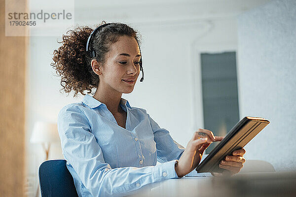 Lächelnder Kundendienstmitarbeiter mit Tablet-PC am Schreibtisch im Büro