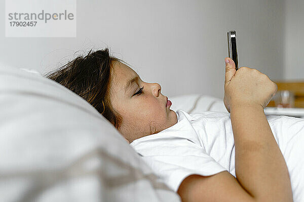 Mädchen benutzt Mobiltelefon und liegt zu Hause im Bett