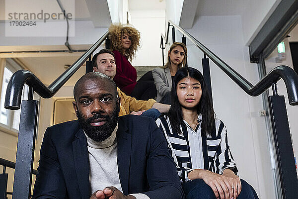 Gruppe junger Geschäftsleute sitzt auf Treppen in Büroräumen