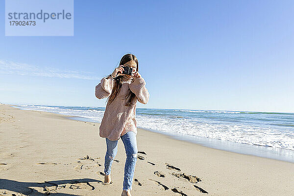 Mädchen rennt und klickt am Strand auf Fotos von der Kamera