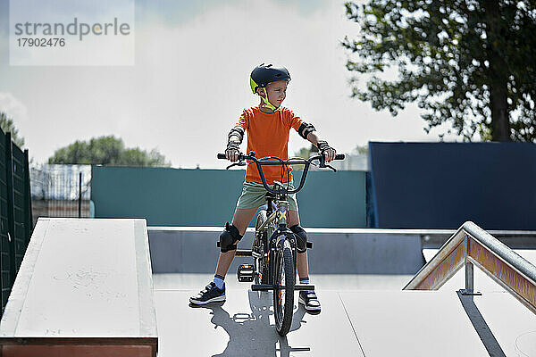 Junge mit Schutzausrüstung sitzt auf einem BMX-Fahrrad im Skateboardpark