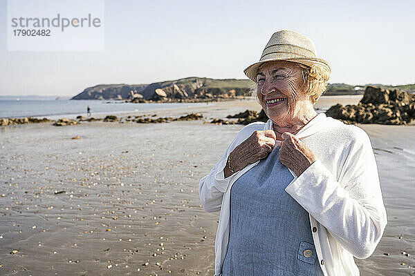 Glückliche ältere Frau mit Hut im Urlaub am Strand