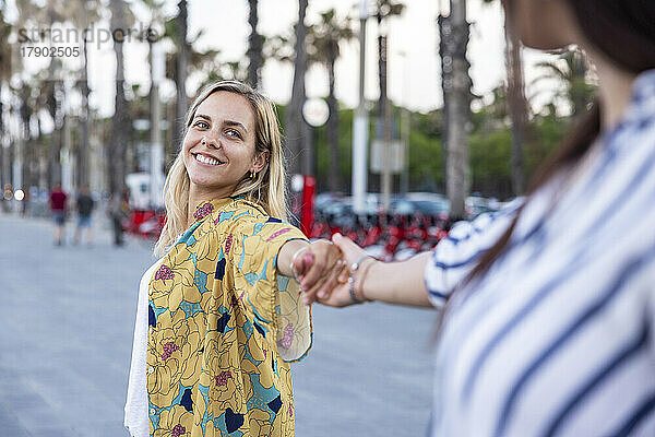 Smiling blond woman holding hand of friend at promenade
