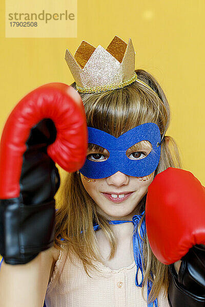 Girl wearing boxing gloves and mask against yellow background