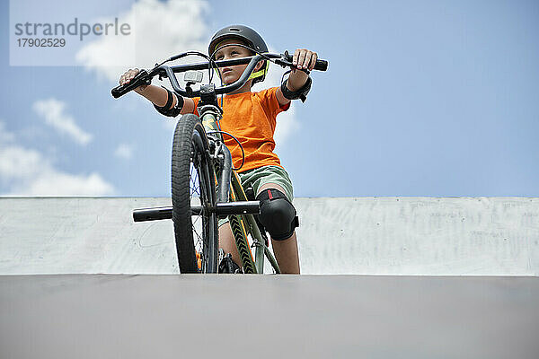 Junge sitzt auf einem BMX-Fahrrad an der Sportrampe