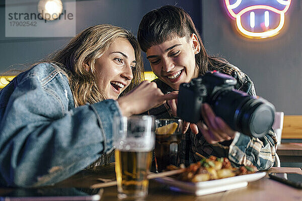 Glückliches lesbisches Paar  das die Kamera teilt und am Tisch im Restaurant sitzt