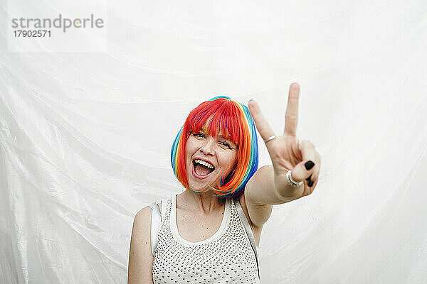 Glückliche Frau mit bunt gefärbten Haaren zeigt eine Friedenszeichen-Geste