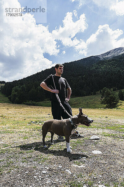 Mann steht an sonnigem Tag mit Hund vor Berg
