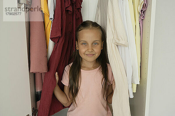 Girl with eyes closed sitting by clothes in closet