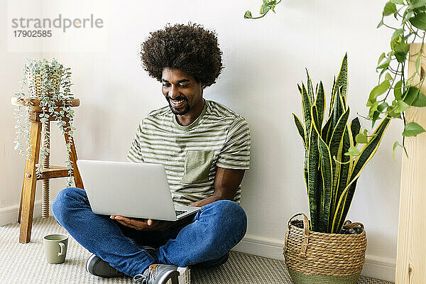 Glücklicher Mann mit Laptop  der zu Hause vor der Wand sitzt