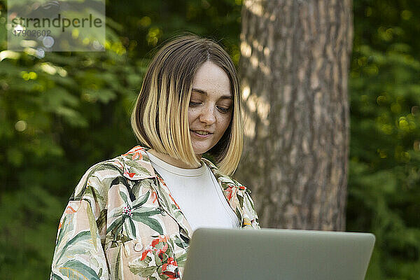 Junge Frau arbeitet im Park am Laptop