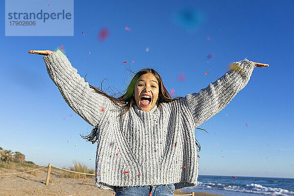 Excited girl throwing confetti at beach