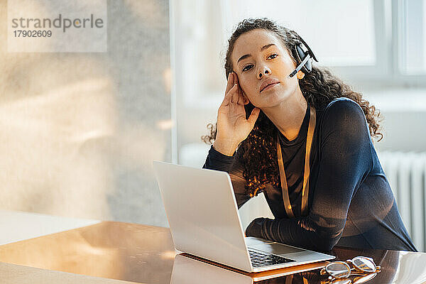 Nachdenklicher Kundendienstmitarbeiter sitzt mit Laptop am Schreibtisch im Büro