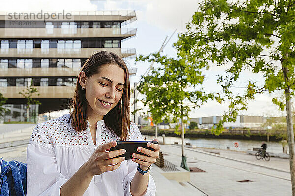 Lächelnde Frau benutzt Smartphone vor Gebäude