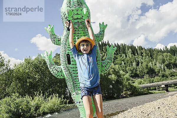 Fröhlicher Junge hält an einem sonnigen Tag ein aufblasbares Krokodil