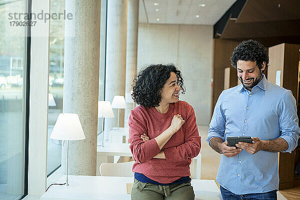 Glücklicher Mann und Frau diskutieren über Tablet-PC in der Bibliothek