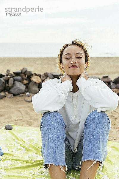Lächelnde Frau sitzt mit geschlossenen Augen und genießt den Strand