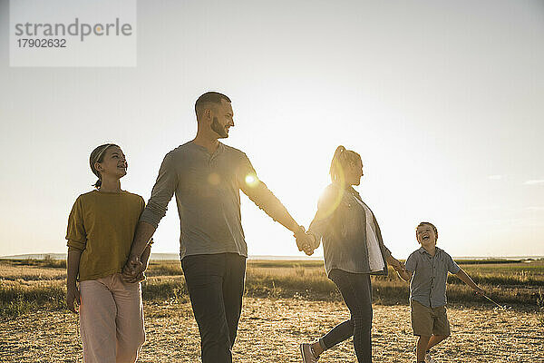 Selbstbewusste Familie geht bei Sonnenuntergang Händchen haltend zusammen spazieren