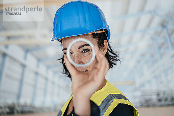 Lächelnder Ingenieur schaut durch ringförmiges Objekt in der Fabrik