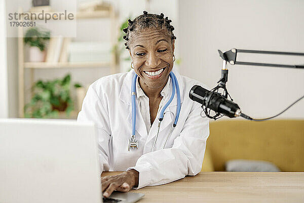 Lächelnde Ärztin mit Mikrofon und Laptop im Heimbüro