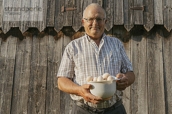 Älterer Bauer hält an einem sonnigen Tag eine Schüssel mit Eiern