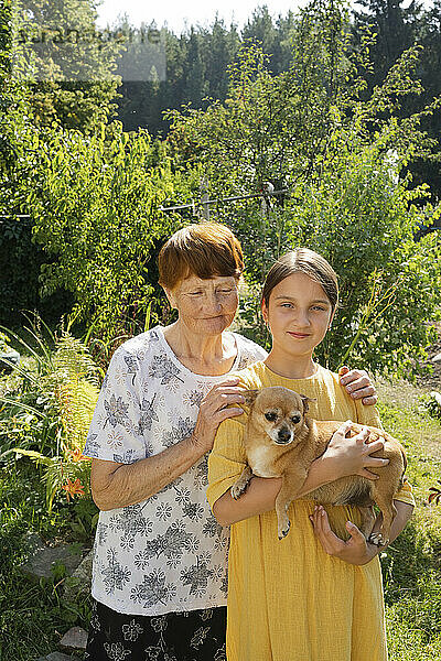 Großmutter und Enkelin stehen mit Hund im Garten