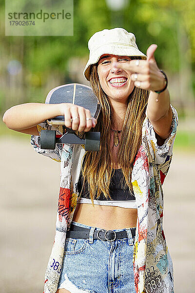 Fröhliche Frau mit Skateboard zeigt Mittelfinger