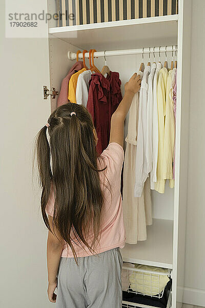 Girl choosing clothes from closet at home