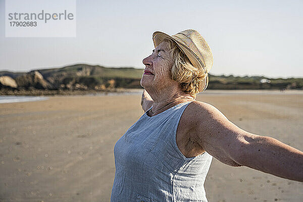 Lächelnde Frau mit ausgestreckten Armen genießt den Strand