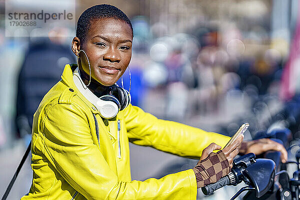 Junge Frau mit Smartphone an der Fahrradstation an einem sonnigen Tag