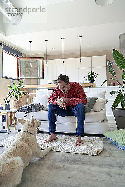 Mann sitzt zu Hause auf dem Sofa vor seinem Hund