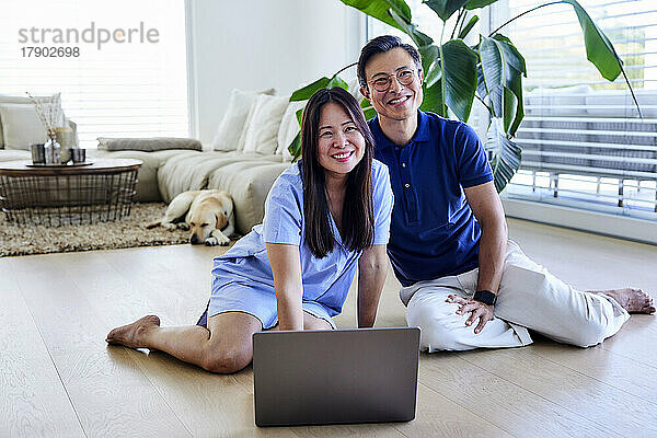 Glückliche Freiberufler mit Laptop  der zu Hause im Wohnzimmer auf dem Boden sitzt