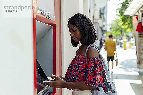 Frau mit Kreditkarte steht am Geldautomaten