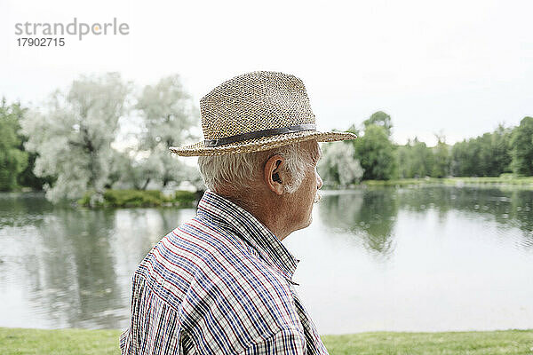 Älterer Mann mit Hut am See im Park