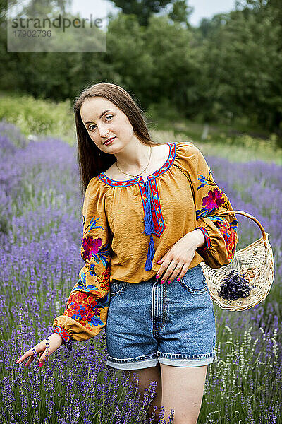 Glückliche Frau mit Korb steht auf der Lavendelfarm