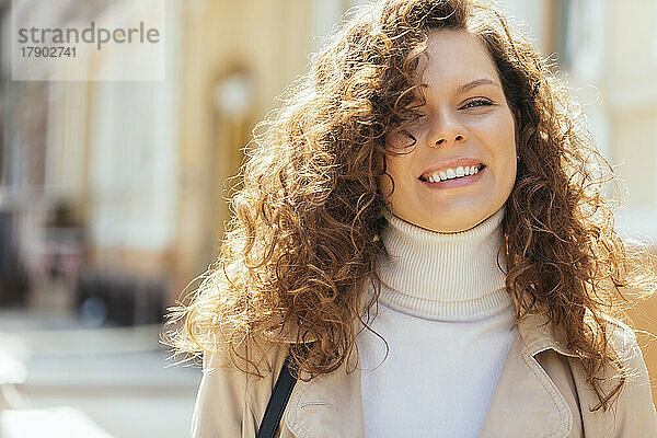 Glückliche Frau mit lockigem braunem Haar an einem sonnigen Tag