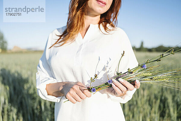 Frau mit Blumen steht im Maisfeld