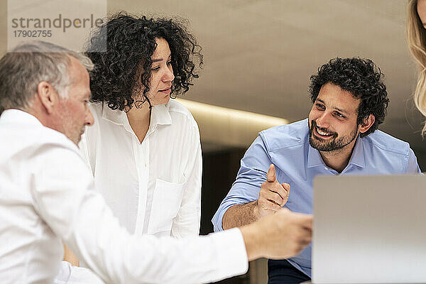 Lächelnder Geschäftsmann diskutiert am Laptop mit Kollegen im Büro