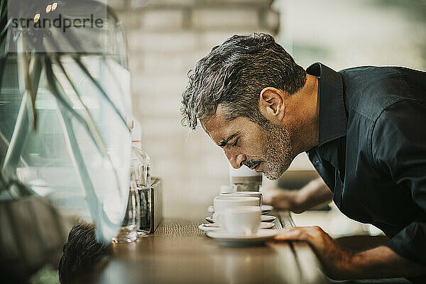 Reifer Mann riecht Kaffee auf dem Tisch im Café