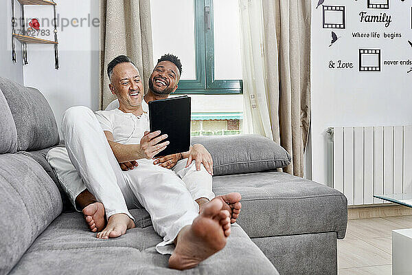 Glückliches Paar sitzt zu Hause auf dem Sofa und benutzt einen Tablet-PC