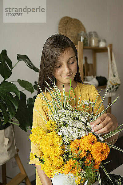 Lächelndes Mädchen  das zu Hause Blumen in einer Vase berührt