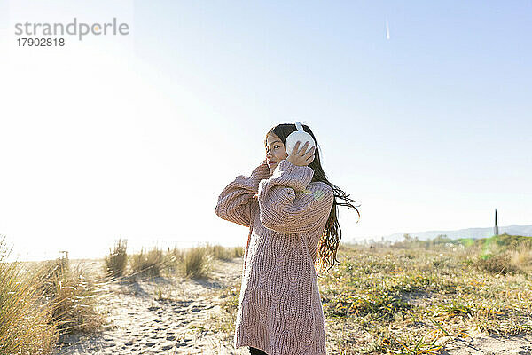 Mädchen trägt Ohrenschützer am Strand an einem sonnigen Tag