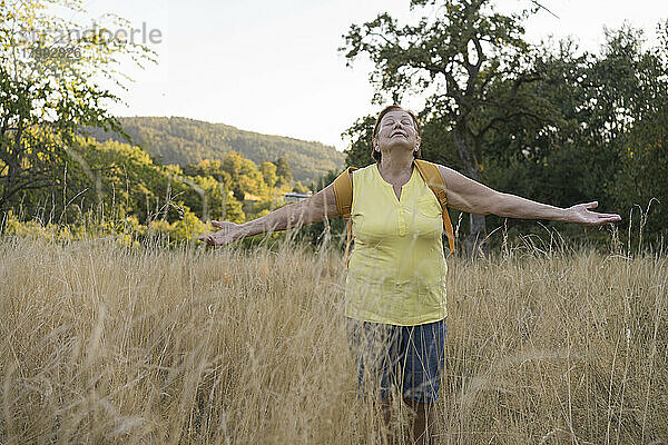 Senior woman with arms outstretched standing in field