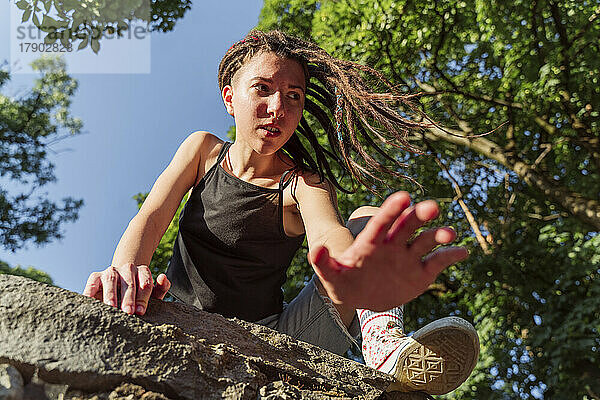 Nachdenklicher nicht-binärer Mensch mit Loks klettert auf Steinmauer