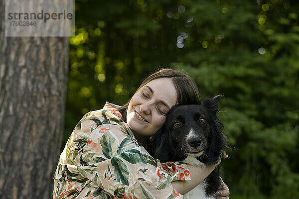 Glückliche junge Frau umarmt Hund im Park