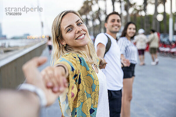 Lächelnde Frau hält Händchen von Freunden und genießt die Promenade