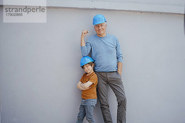 Selbstbewusster älterer Mann und Junge mit Schutzhelm vor der Wand