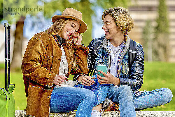 Fröhliche Freunde  die auf der Bank sitzen und Musik über ihr Smartphone hören