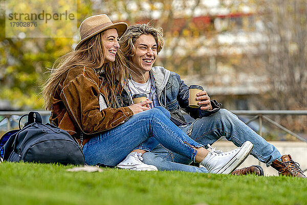 Fröhliche Touristen mit Einwegbechern sitzen im Park